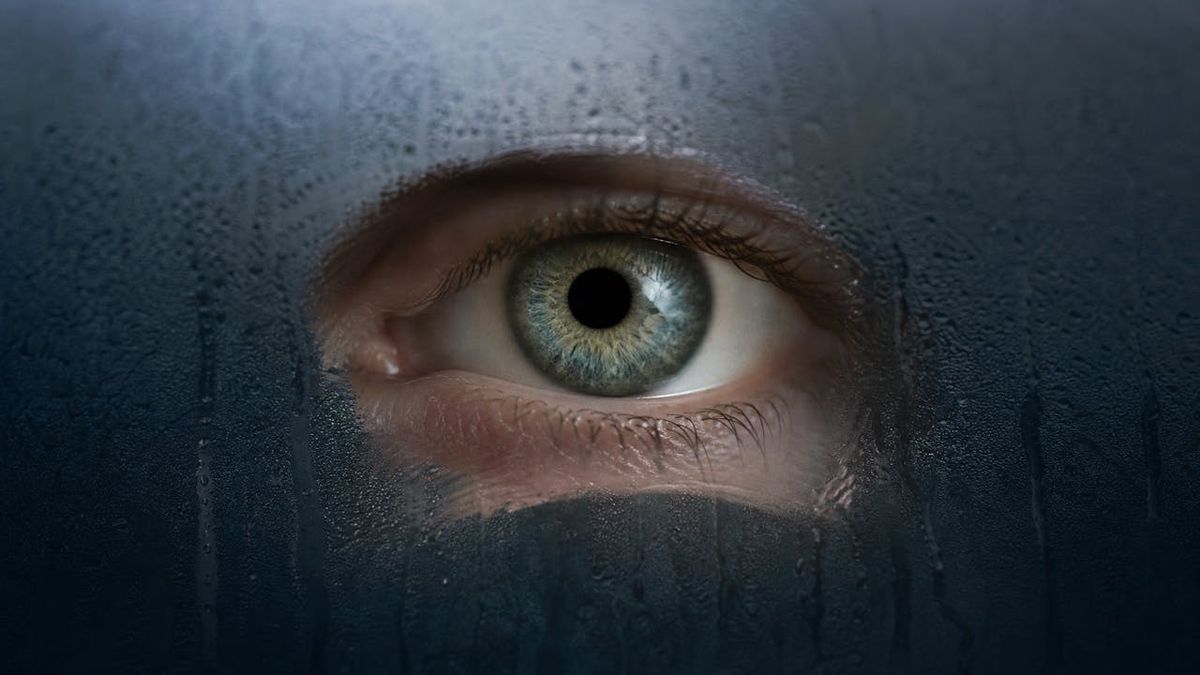 An eye seen through a fogged pane of glass with one clear wiped patch
