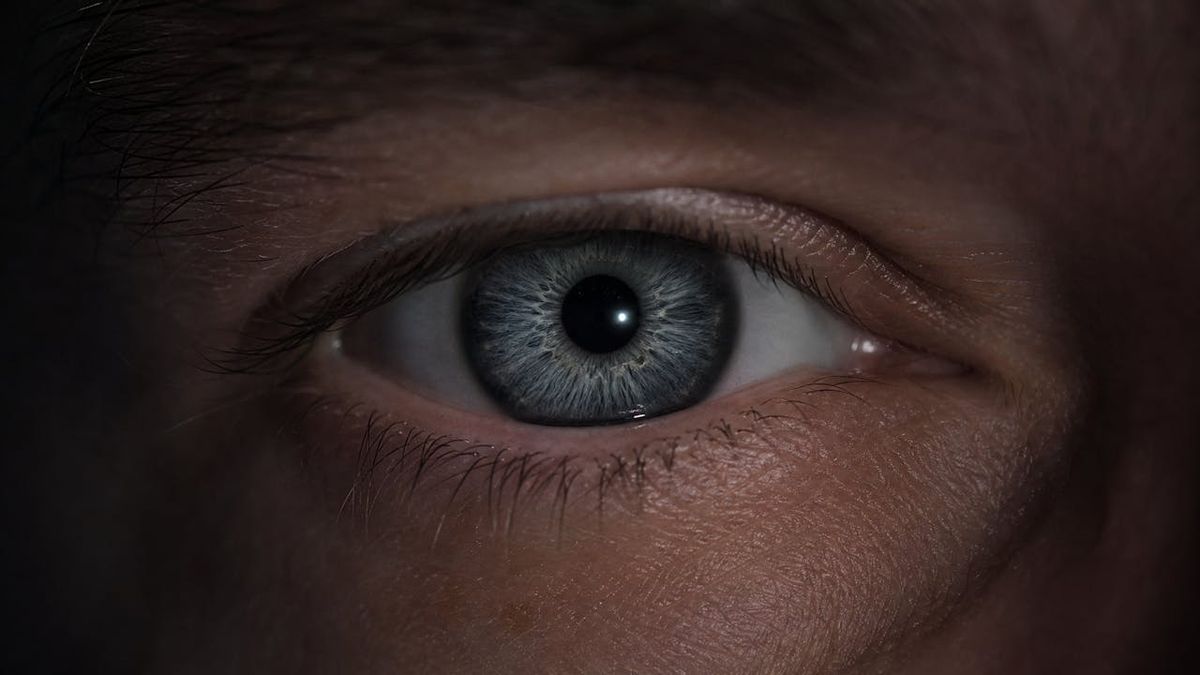 Close-up of an eye in dim light with a bright point of light glinting from inside the pupil