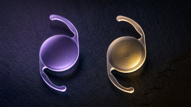 A smooth lens implant under violet light beside a ringed trifocal lens implant under gold light