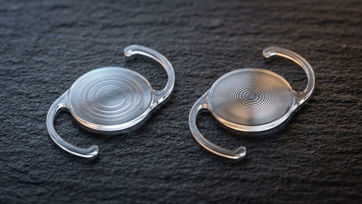 Two trifocal intraocular lens implants side by side on a dark surface, each a round ringed optic with two curved haptic arms