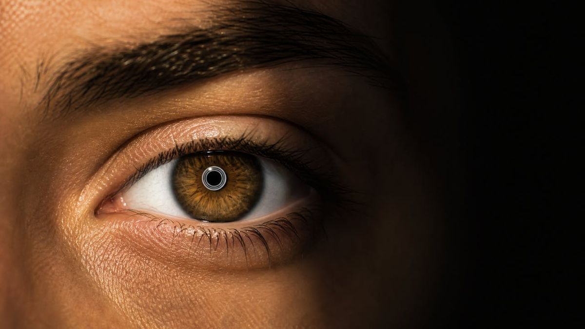 Close-up of a brown eye with a faint ring reflection inside the pupil, half in shadow
